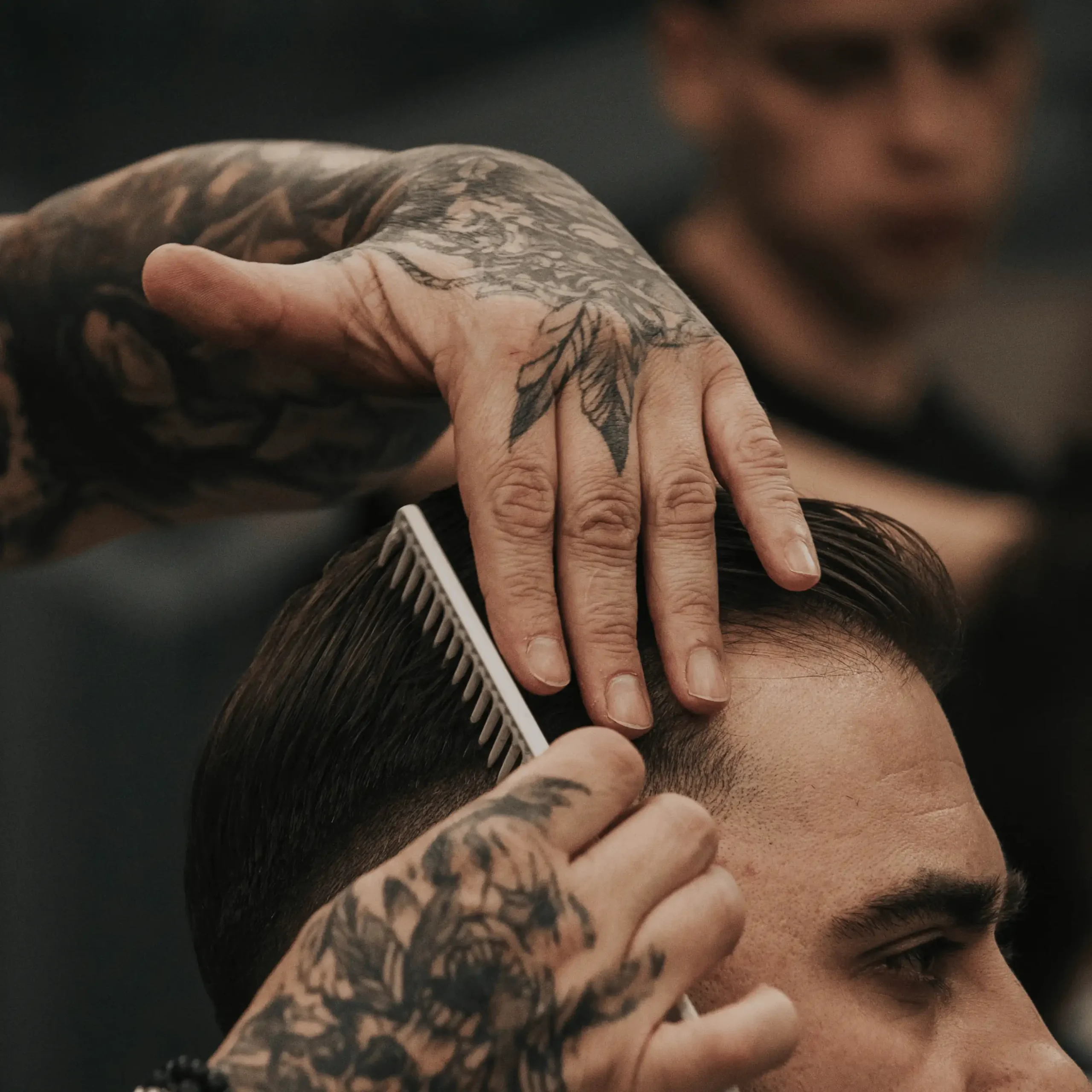 Barber układający fryzurę klientowi przy pomocy grzebienia.