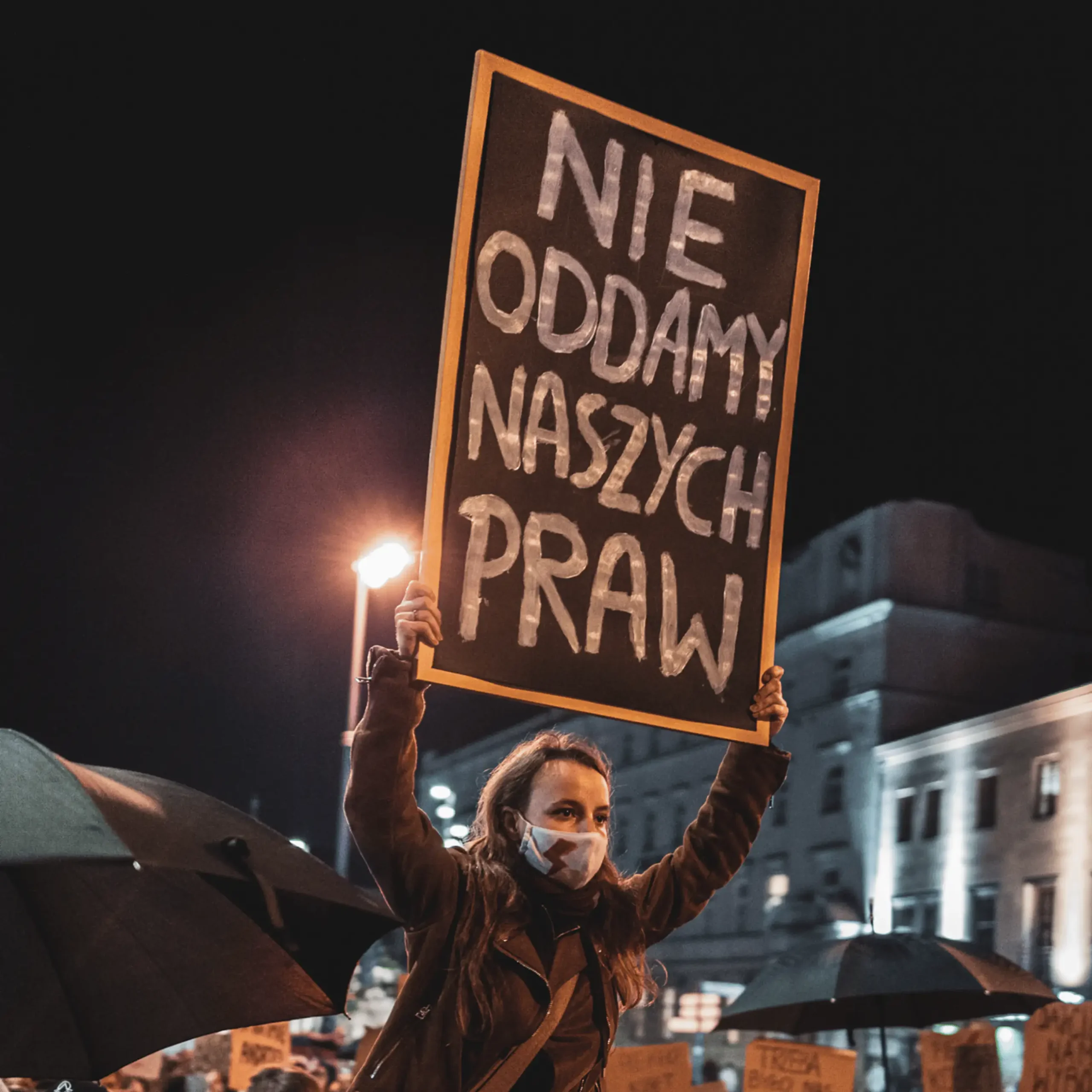Kobieta z maseczką na twarzy i transparentem na strajku kobiet.